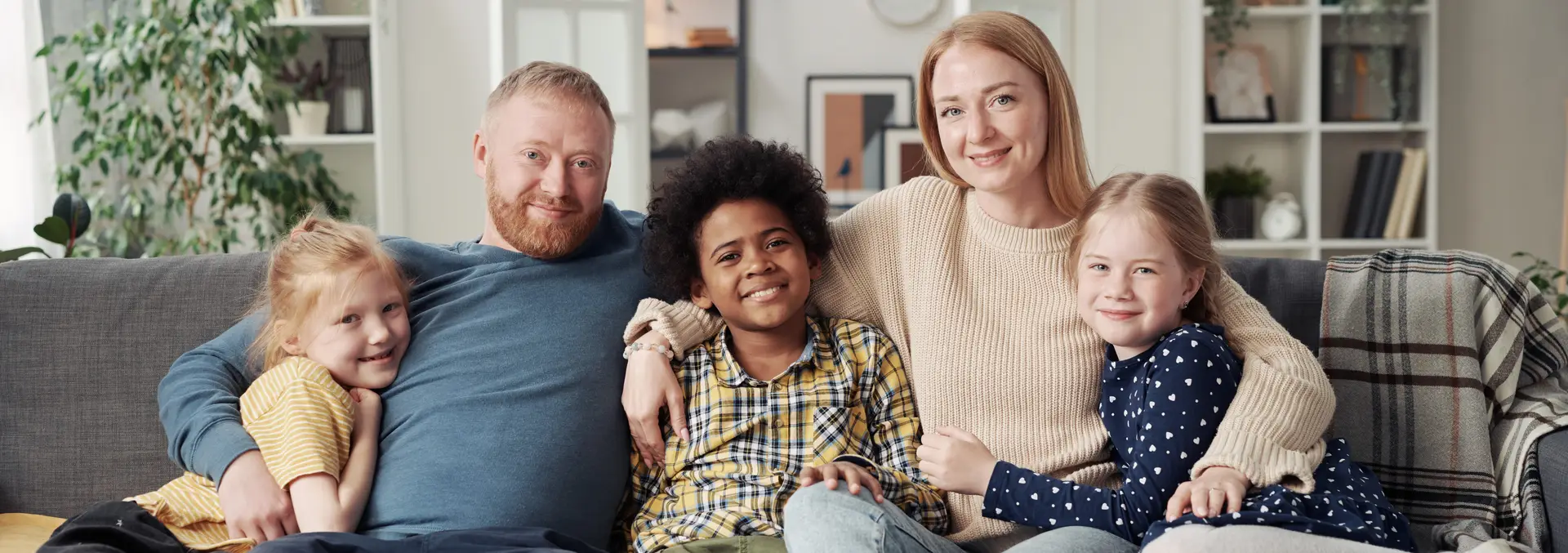 Happy adoptive family with children at home Portrait of happy adoptive family with their children embracing together and smiling at camera while resting on sofa in living room